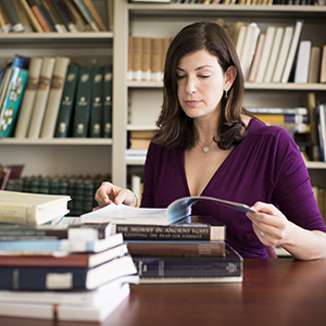 "woman reading through a pile of books"