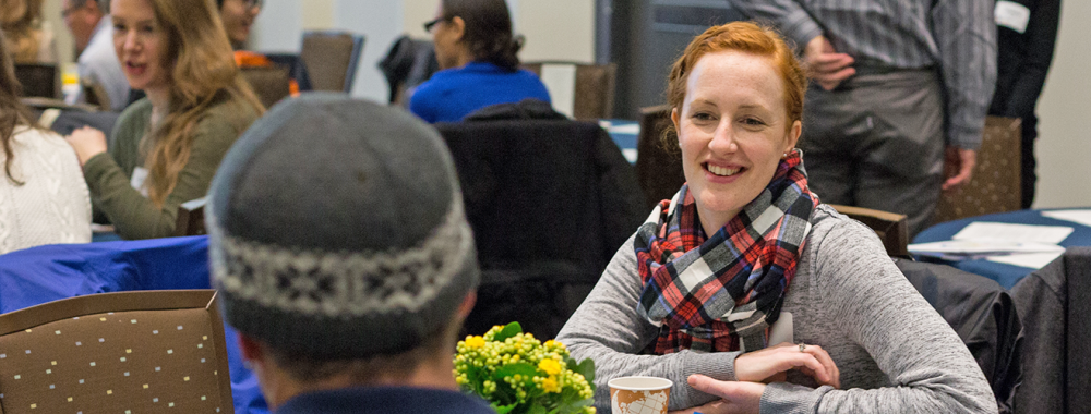 woman at a table smiling as she listens to someone