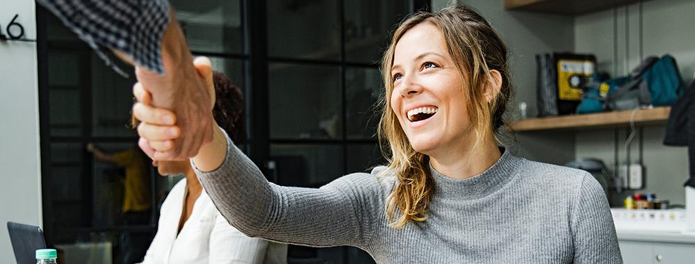 woman looking up at a colleague and smiling while they shake hands