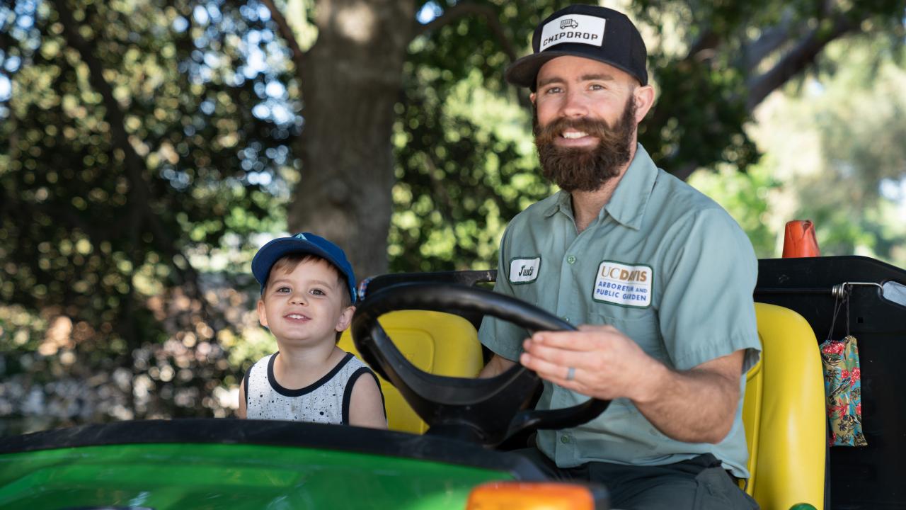 Employee driving tractor with young child beside him