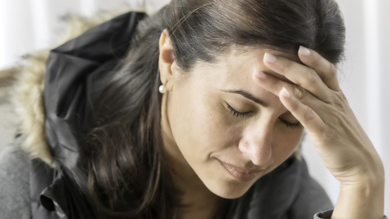 Woman is holding her head in her hand, looking down.  