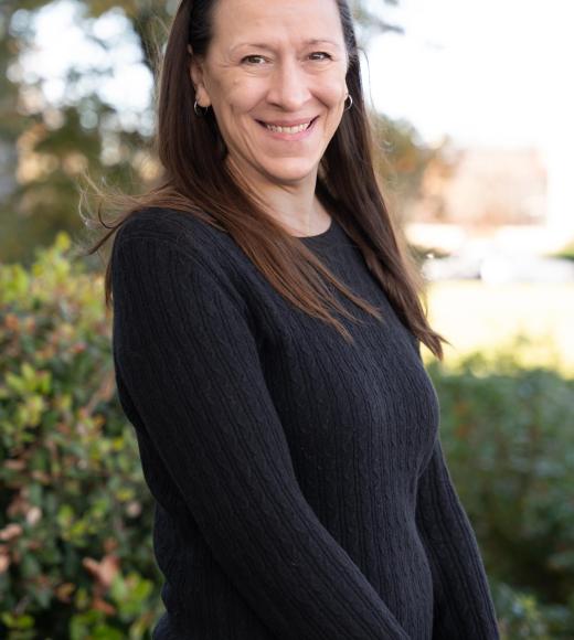 An wearing black top with hair down, trees in background