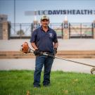 UC Davis Grounds employee in front of UC Davis Health Stadium with a weedwhacker in hand. 