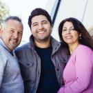 A father, adult son, and mother standing together and smiling.