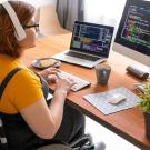 Person sitting in wheelchair at a desk, looking at a computer monitor and wearing headphones. 