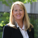 Blonde woman in suit stands in front of greenery