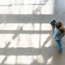 Woman is walking holding a tablet, looking down.  