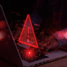 A person typing on a laptop with a red warning alert floating above the keys.