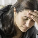 Woman is holding her head in her hand, looking down.  